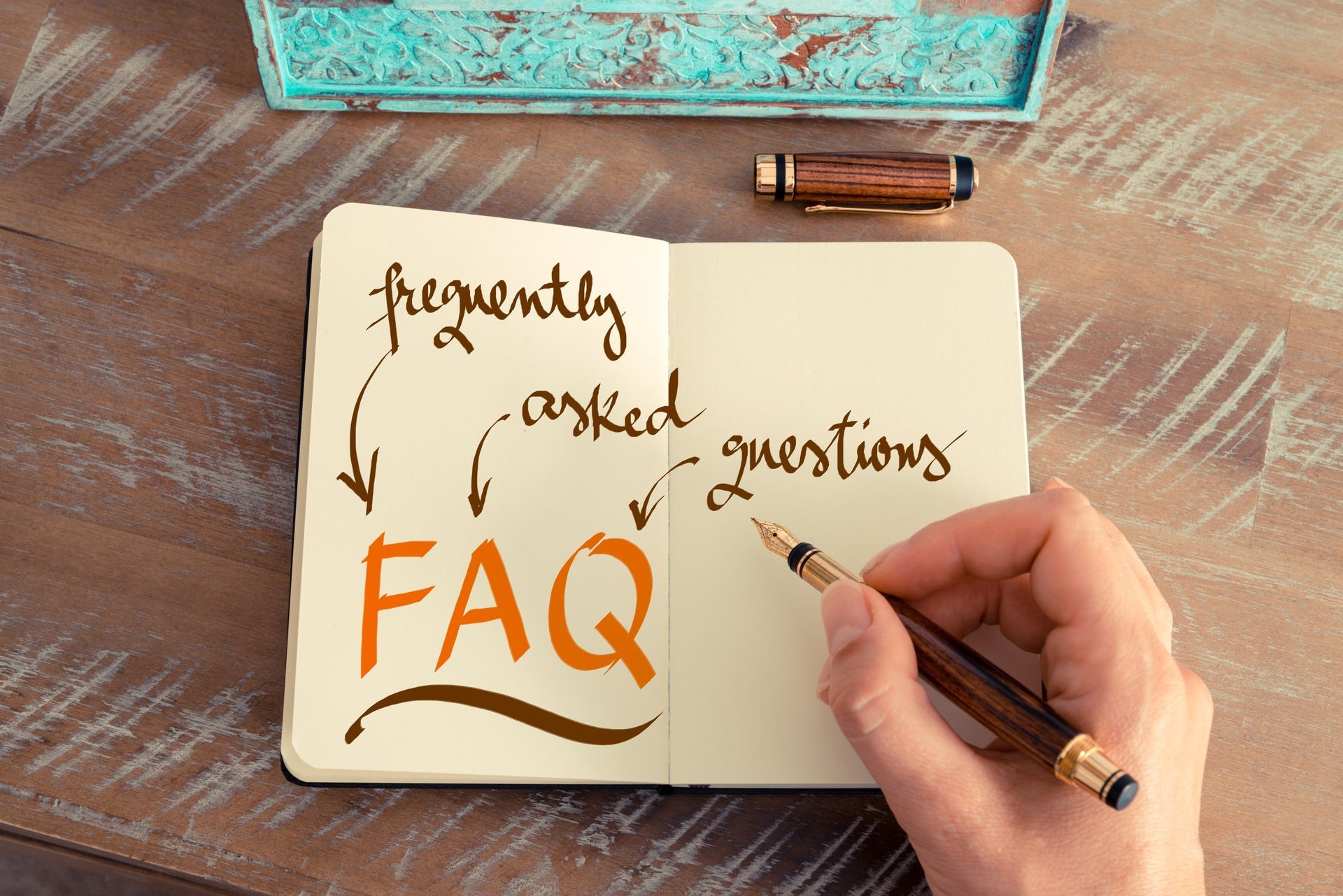 Retro effect and toned image of a woman hand writing a note with a fountain pen on a notebook. Handwritten text FAQ FREQUENTLY ASKED QUESTIONS, business success concept
